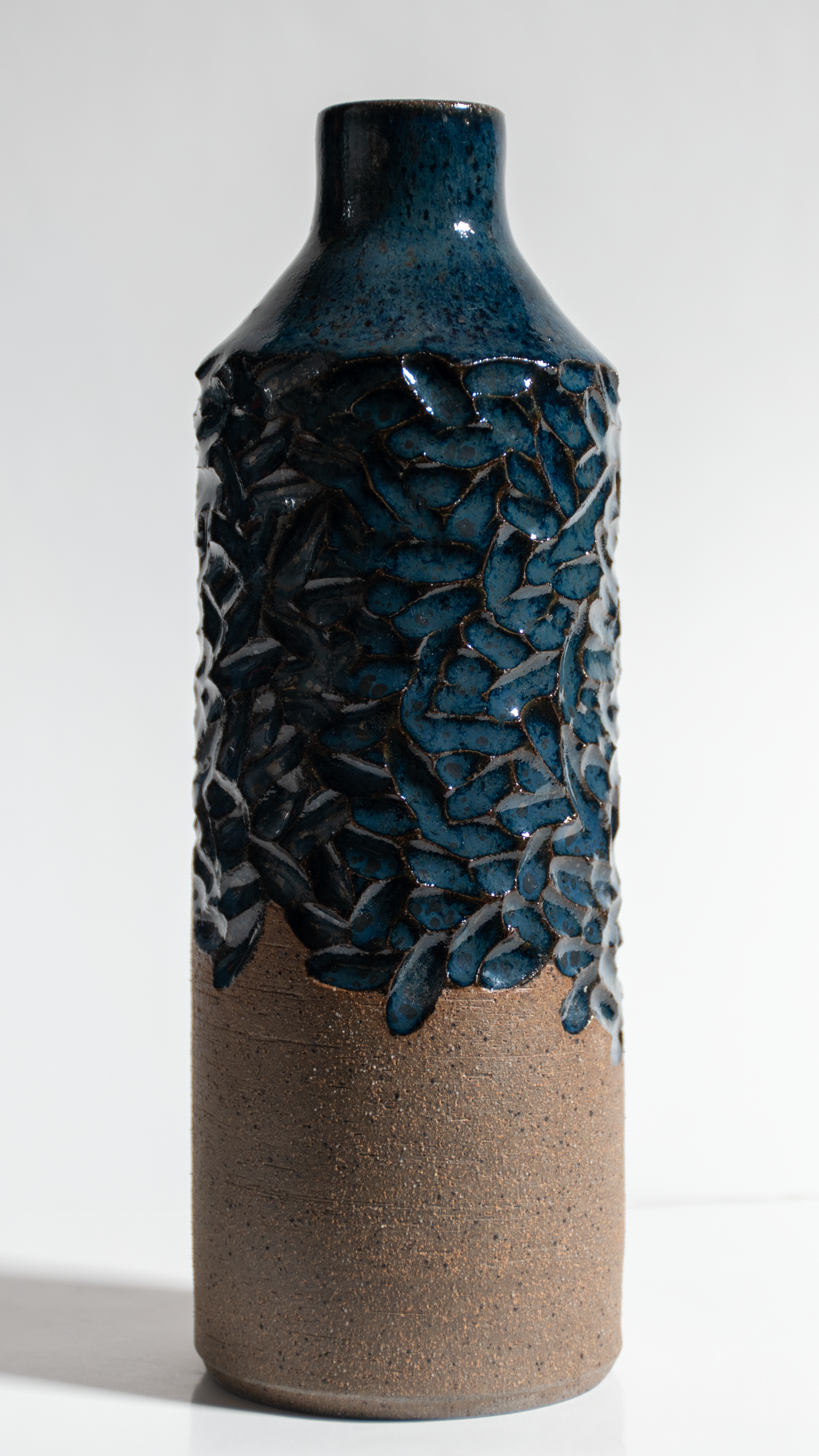 Handmade ceramic Oil bottle, made from tan stoneware clay with a steel blue glaze over the top of carving